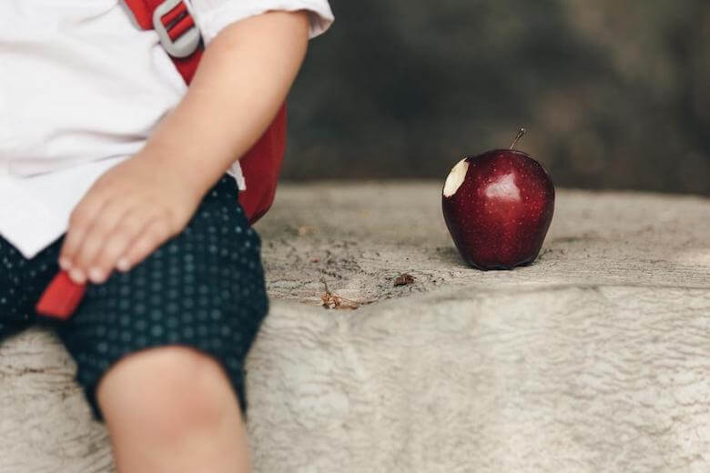boy sitting outdoors next to apple with bite in it - help picky eaters in preschool article image