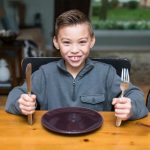 Boy at dinner table with empty plate - teach good nutrition in preschool article image