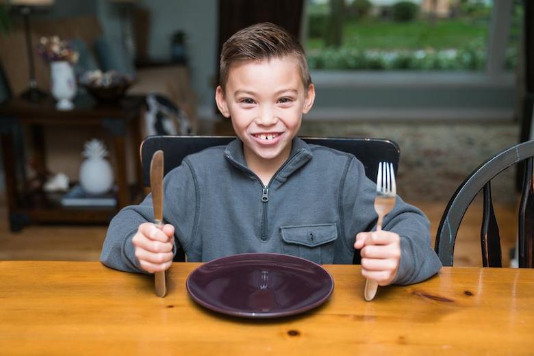 Boy at dinner table with empty plate - teach good nutrition in preschool article image