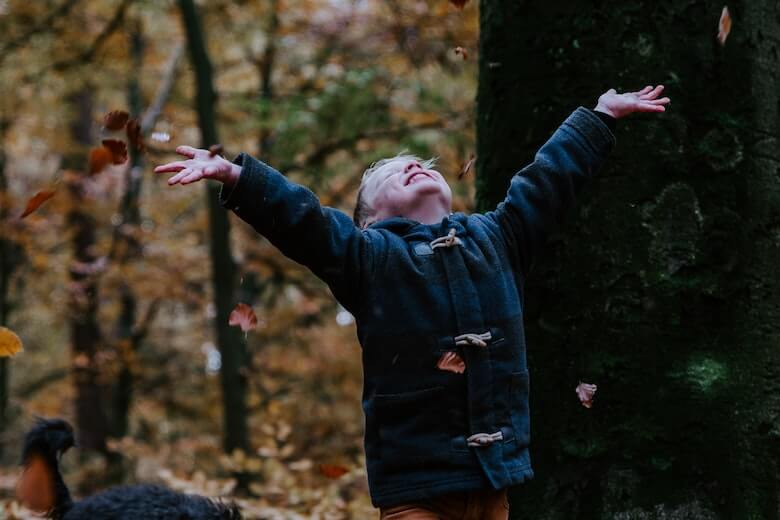 child throwing leaves in forest - gravity game for preschool
