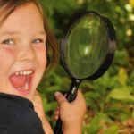 child using magnifying glass happy - sight sensory idea infant daycare