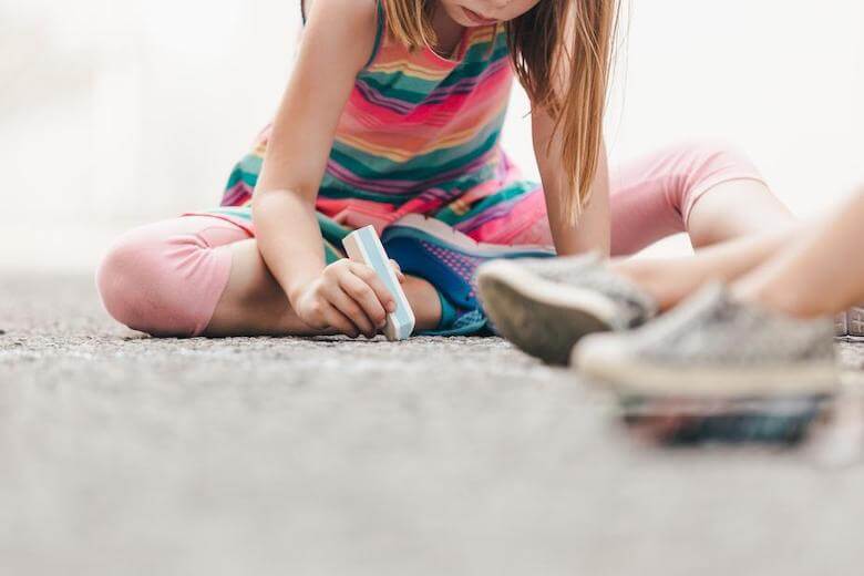 girl drawing on concrete with sidewalk chalk - image for article on benefits of downtime for kids