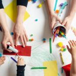 adult and child hands reaching for craft material - benefits of older kids mentoring preschoolers article image