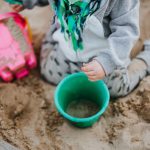 Child playing with buckets in a sandbox for benefits of messy play and dirty play in early childhood or preschool article