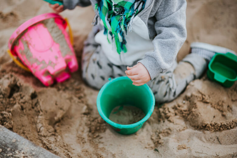 Child playing with buckets in a sandbox for benefits of messy play and dirty play in early childhood or preschool article
