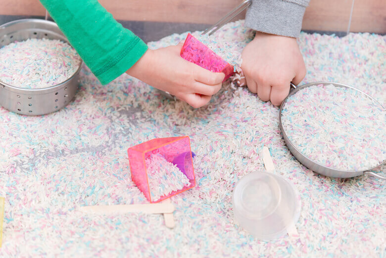 kids hands playing in rice sandbox for sensory development skills at daycare