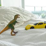 toy dinosaur and car on parents bed - types of play in childhood article image